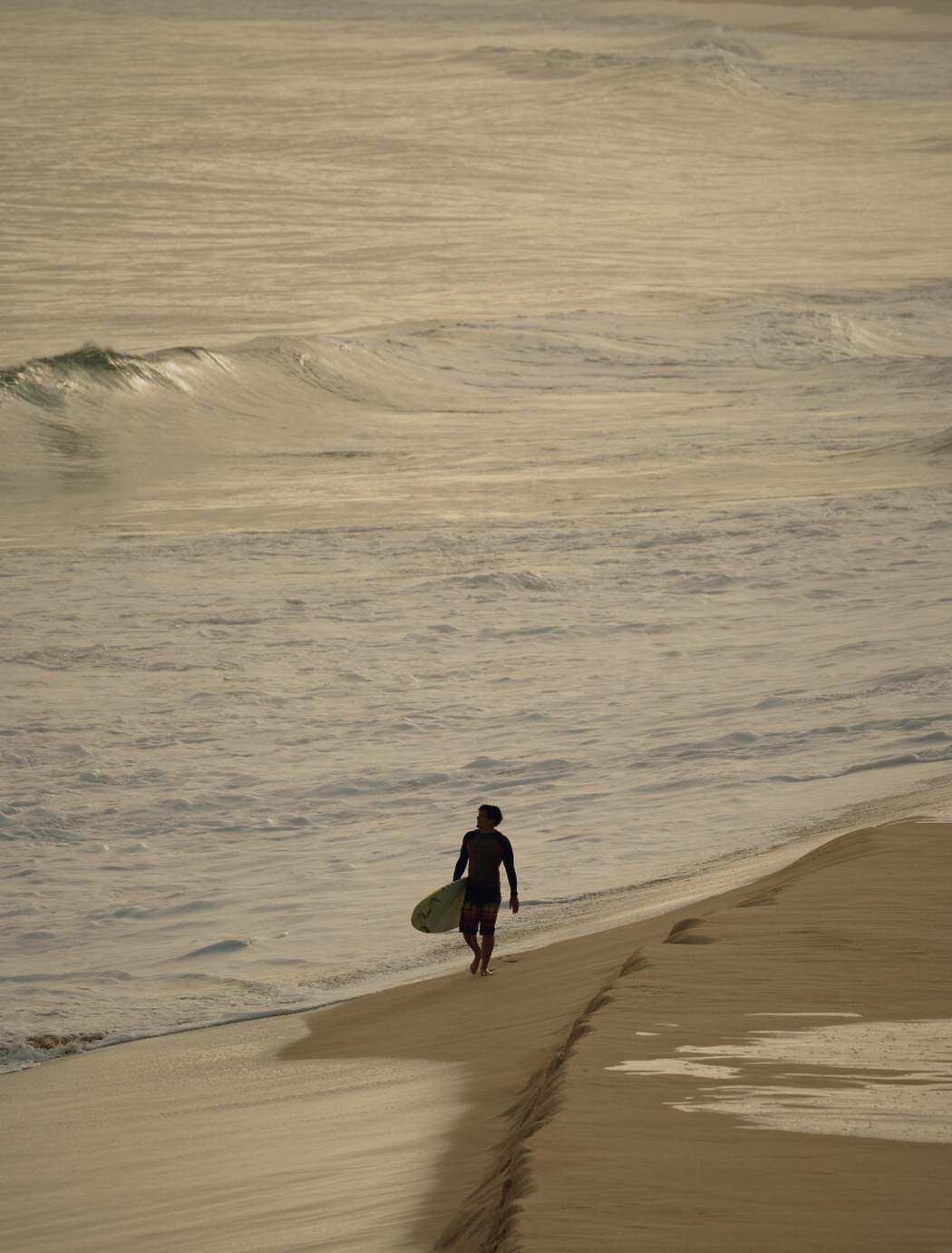 A lone figure walking the shoreline in late afternoon light